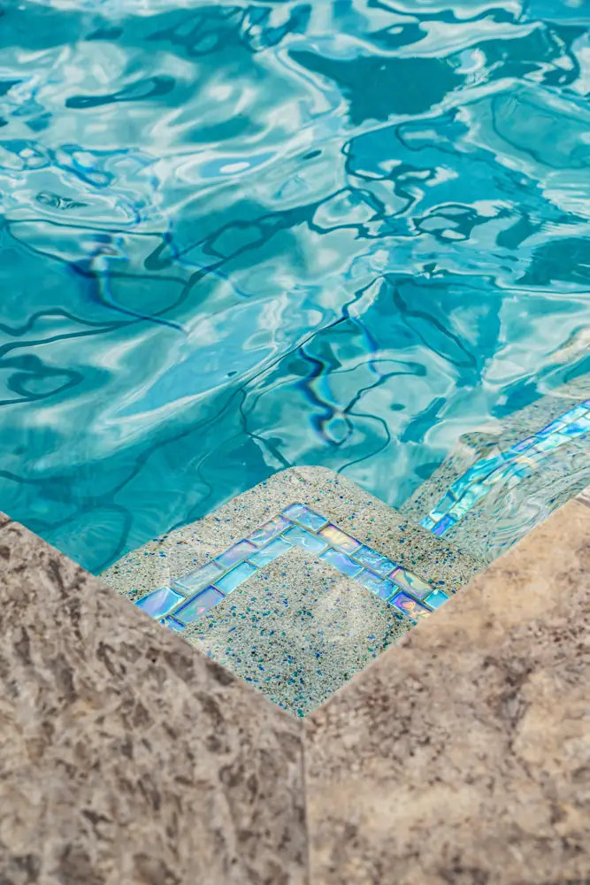 Pool steps with iridescent tile trim and marble coping