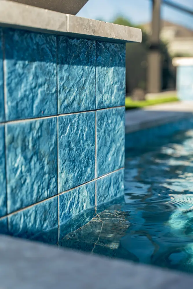 Textured blue tile wall and coping beside the pool
