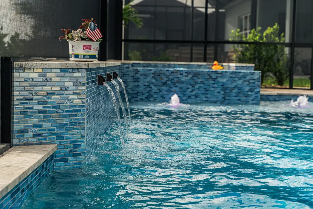 Tile-wall waterfall scuppers spilling into a screened pool — Clermont, Florida